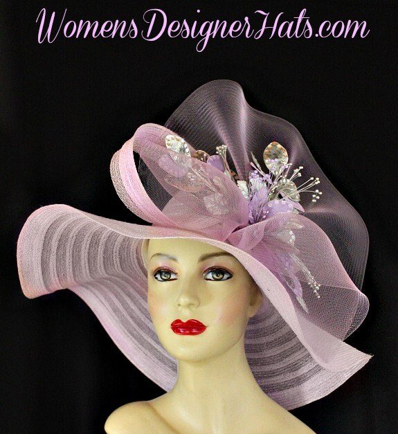 Ladies Haute Couture Soft Pastel Lilac Purple Splash Of Grape Lavender Designer Wide Brim Kentucky Derby Hat. This Custom Made Fashion Hat Is Trimmed With A Large Bow Made Of The Same Material Of The Hat And A Large Sheer Pastel Purple Crinoline Bow. Placed Within The Bow Are Hand Dyed And Sprayed Lavender And Metallic Silver Sequin Velvet Millinery Flowers With Silk Leaves.
