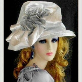 Silver grey ladies designer Church hat. This impressive fashionable hat is adorned with a large bow with pin stripes. This lovely hat is embellished with silver metallic, grey flowers. In the center of these flowers, are satin grey flowers, with white pearls. This hat, represents timeless elegance, at its finest.